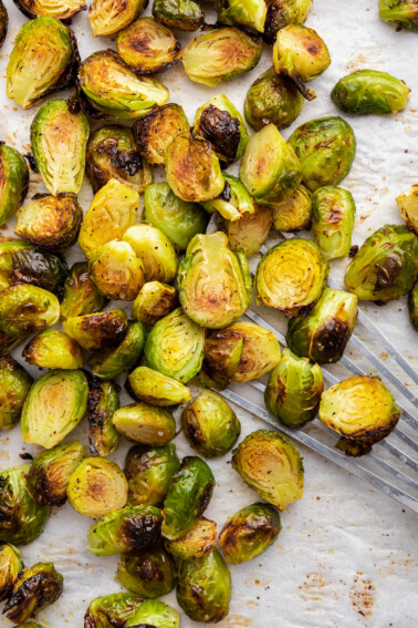 Roasted brussels sprouts on parchment paper on a baking tray with a spatula.