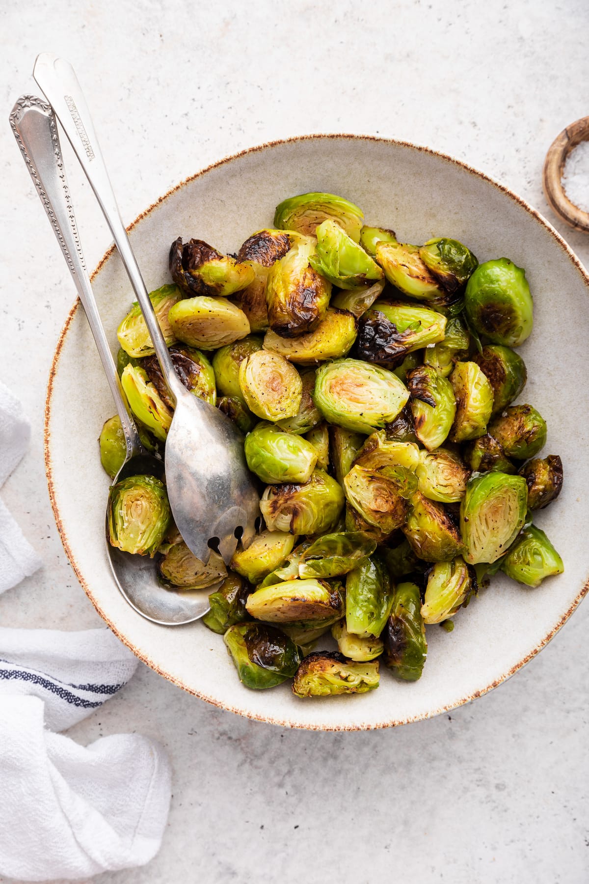 Roasted brussels sprouts in a large bowl with two metal serving spoons.