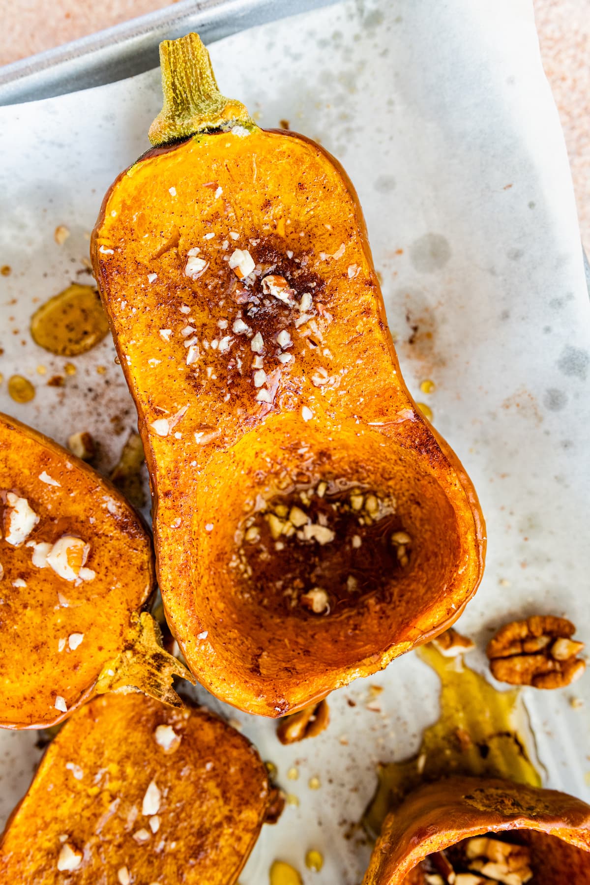 Half of a roasted honeynut squash on a baking tray topped with maple syrup, crushed pecan, and sea salt.