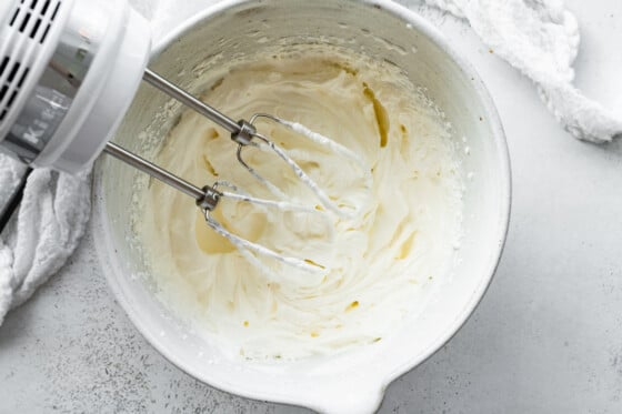 A standing mixer in a large bowl of whipped yogurt and cream cheese.
