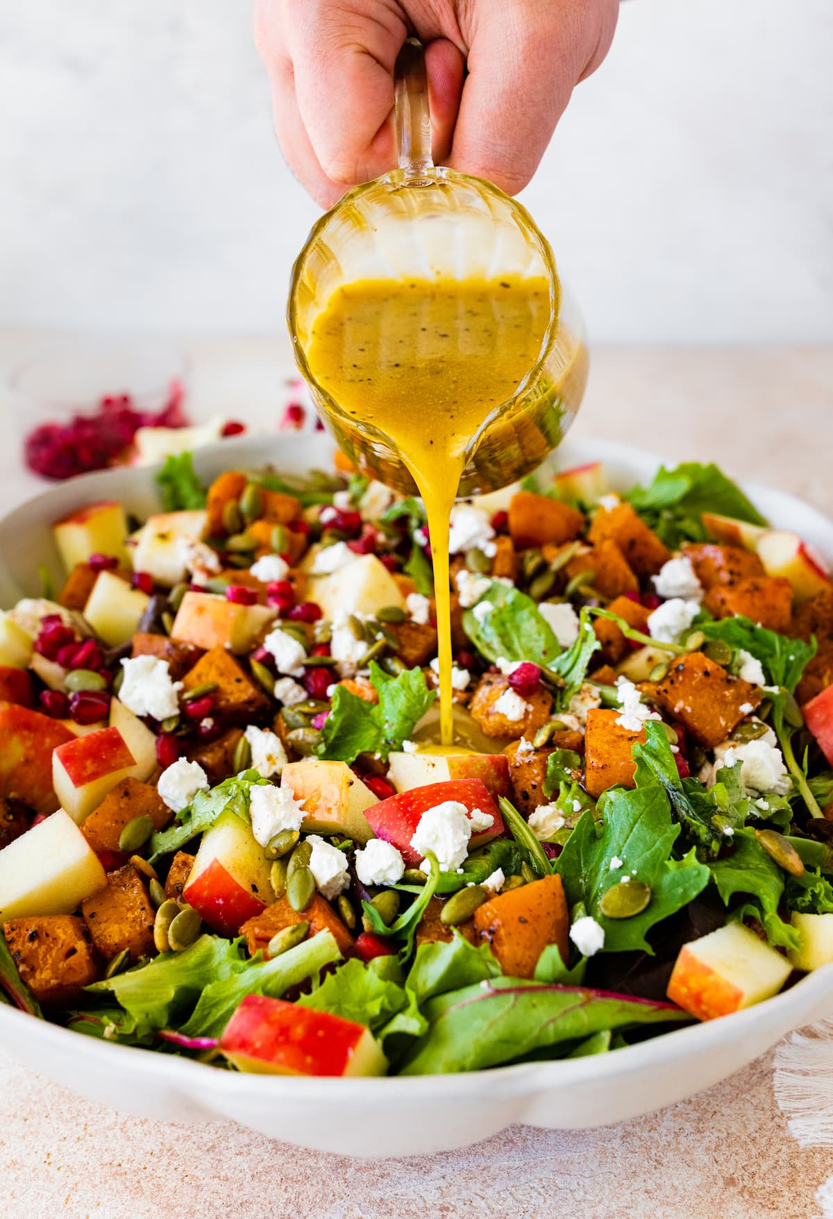 A woman's hand holding and pouring a container of dressing over a large bowl of thanksgiving salad.
