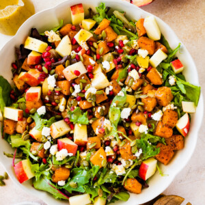 A large bowl of Thanksgiving salad with some noticeable ingredients including pomegranate, diced apple, spinach, pumpkin seeds, and more.