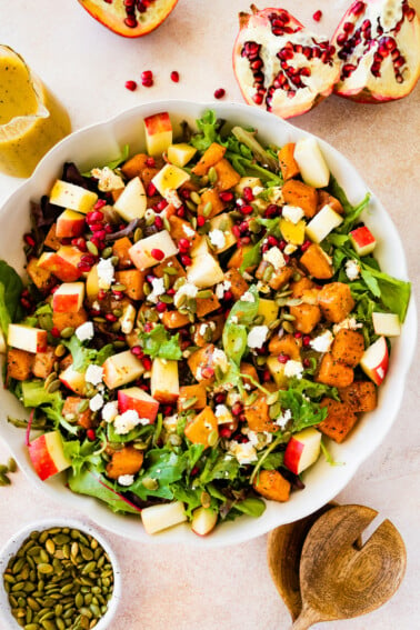 A large bowl of Thanksgiving salad with some noticeable ingredients including pomegranate, diced apple, spinach, pumpkin seeds, and more.