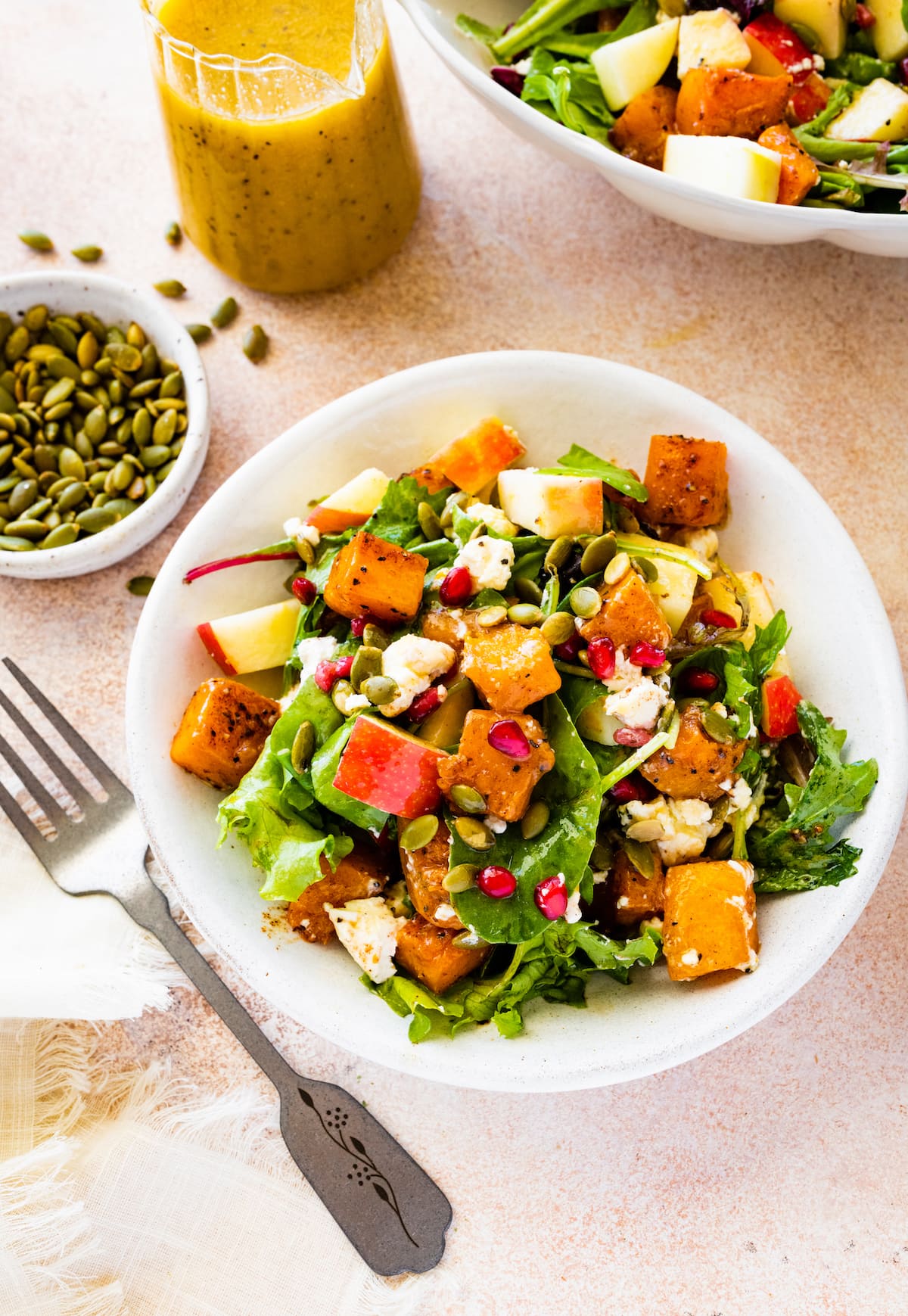 A small bowl of thanksgiving salad with some noticeable ingredients including pomegranate, diced apple, spinach, pumpkin seeds, and more.