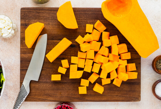 Butternut squash cut into cubes on a wooden cutting board near a knife.