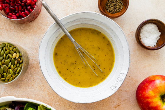 A small metal whisk in a bowl of dressing for a thanksgiving salad.