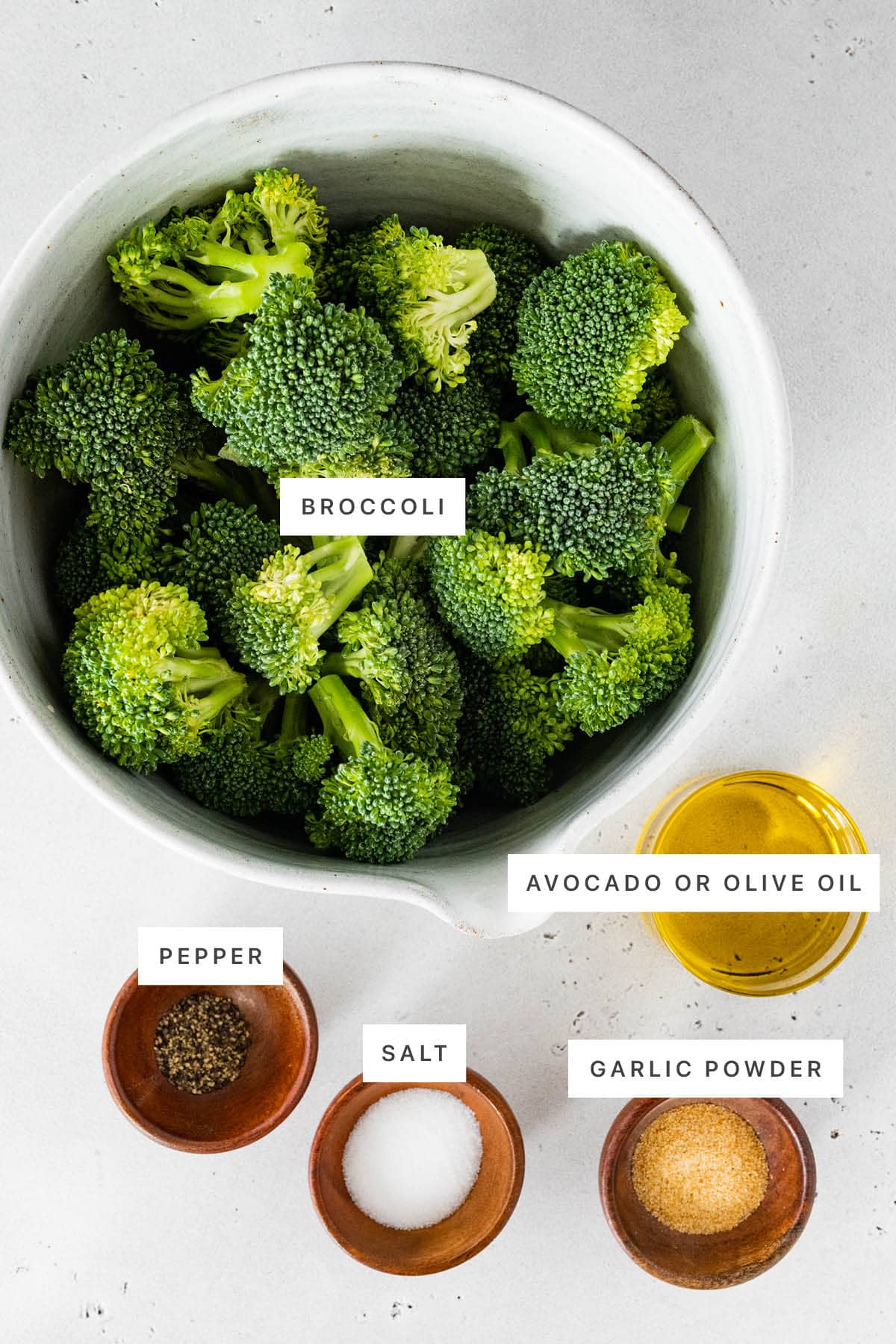 Ingredients measured out to make air fryer broccoli: garlic powder, salt, pepper, olive or avocado oil and broccoli.