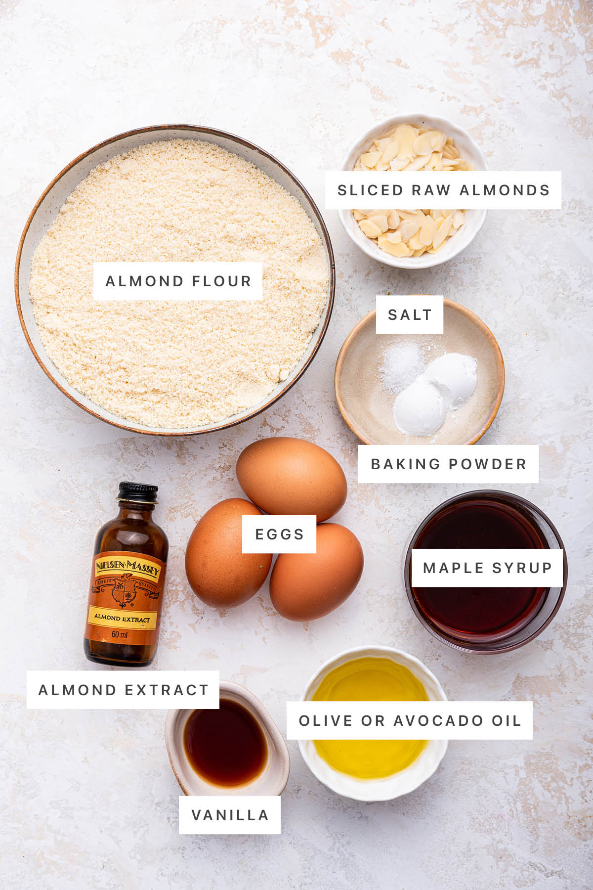 Ingredients measured out to make Almond Cake: almond flour, raw almonds, salt, baking powder, eggs, almond extract, vanilla, oil and maple syrup.