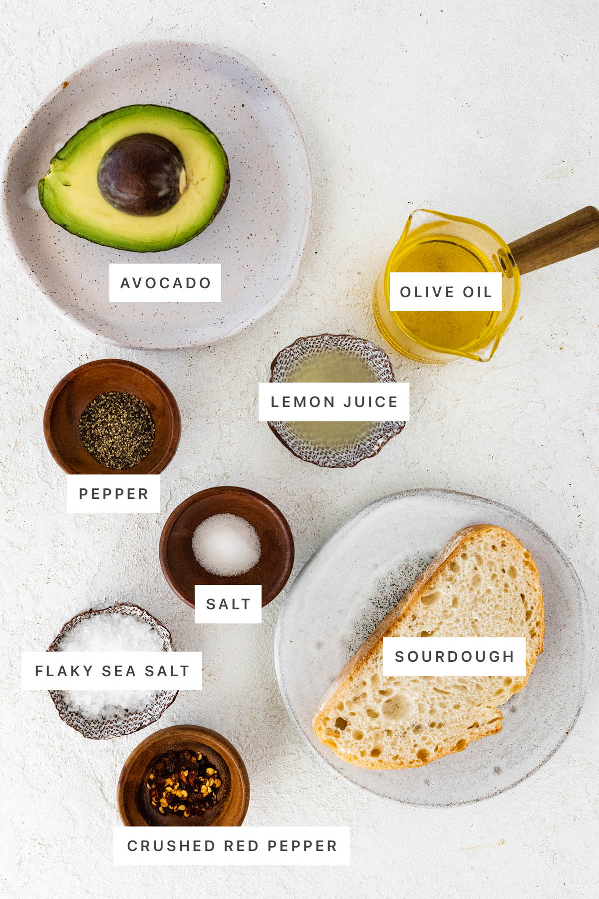 Ingredients measured out to make basic avocado toast: avocado, lemon juice, olive oil, pepper, salt, flaky sea salt, sourdough and crushed red pepper.