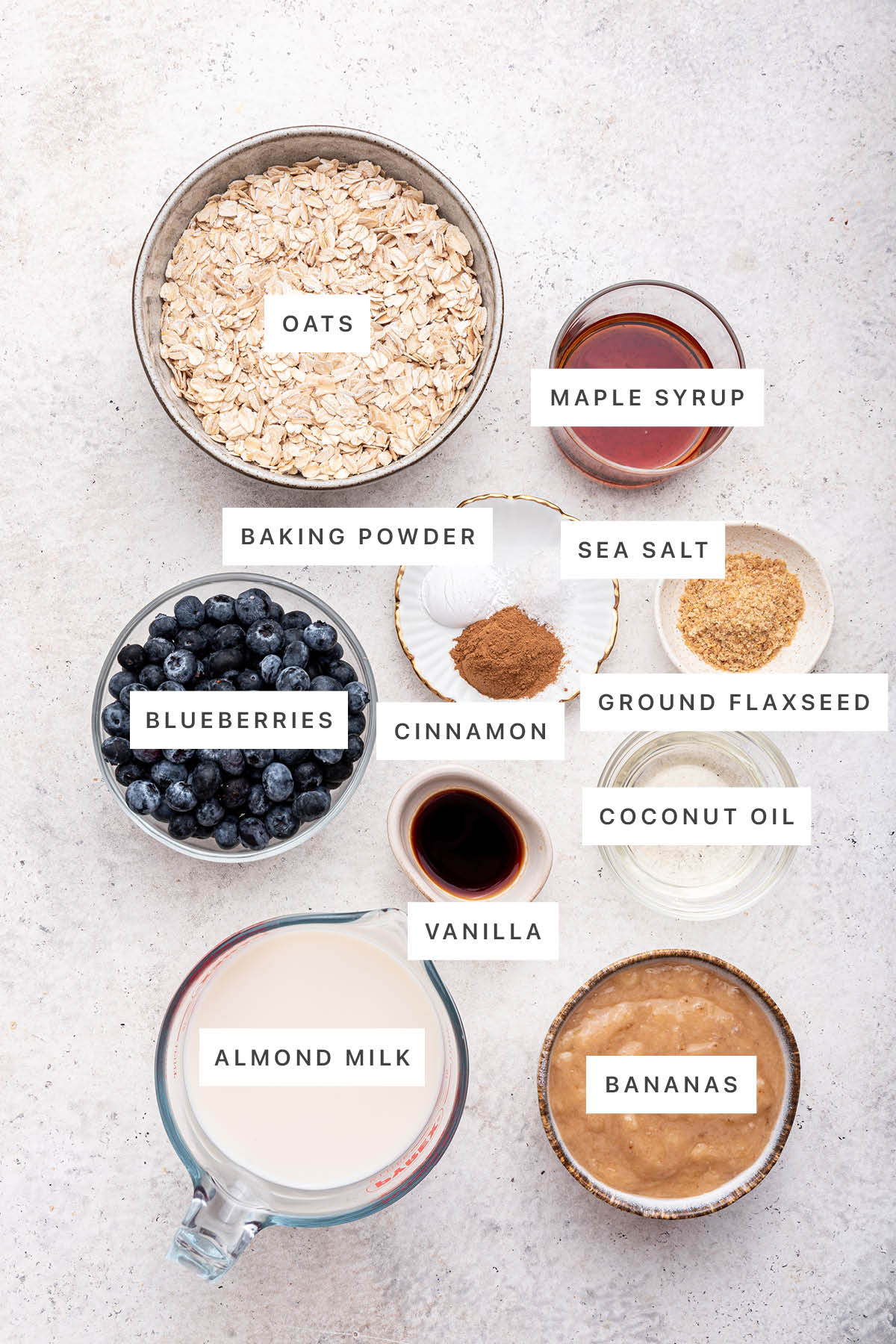 Ingredients measured out to make Blueberry Baked Oatmeal: oats, maple syrup, baking powder, sea salt, cinnamon, ground flaxseed, blueberries, vanilla, coconut oil, almond milk and bananas.