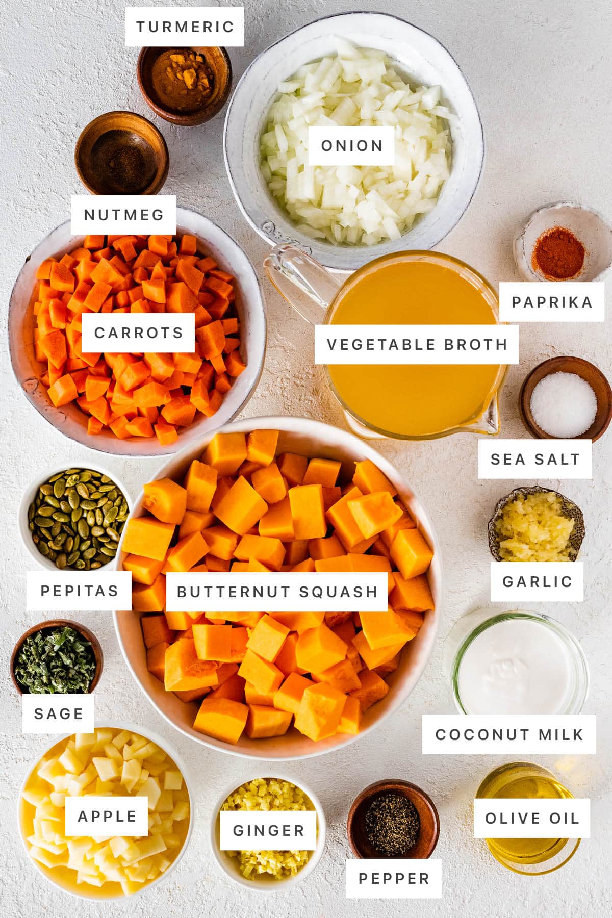 Ingredients measured out to make Butternut Squash Soup: turmeric, onion, nutmeg, carrots, vegetable broth, paprika, sea salt, pepitas, butternut squash, garlic, sage, apple, ginger, pepper, coconut milk and olive oil.