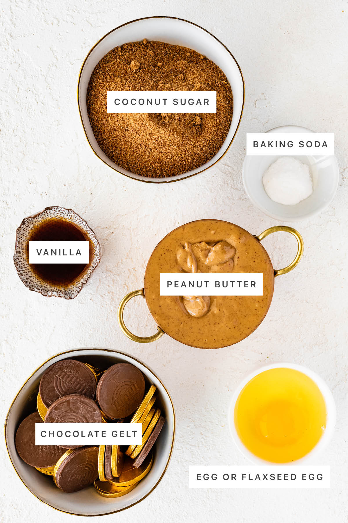 Ingredients measured out to make Hanukkah Gelt Peanut Butter Blossoms: coconut sugar, baking soda, vanilla, peanut butter, chocolate gelt and an egg.
