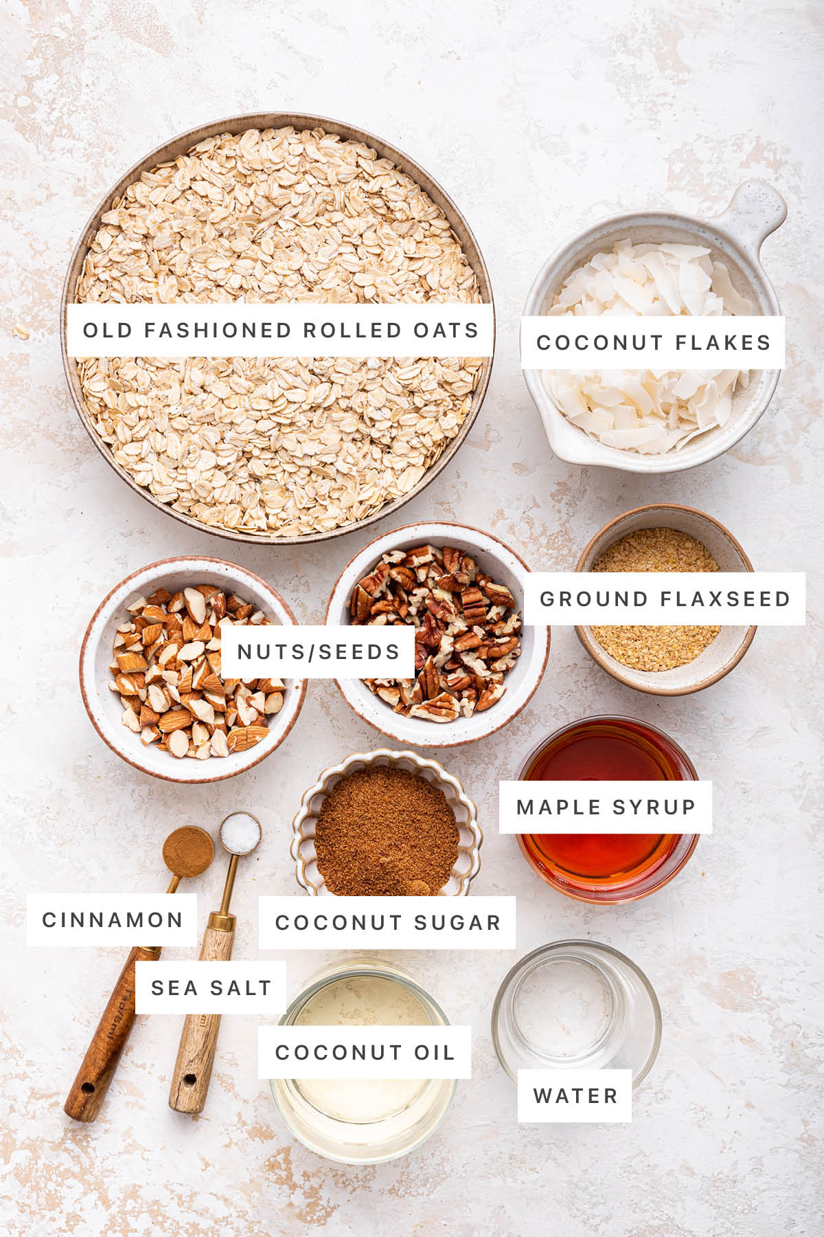 Ingredients measured out to make Homemade Granola: oats, coconut flakes, nuts, ground flaxseed, maple syrup, coconut sugar, cinnamon, sea salt, coconut oil and water.