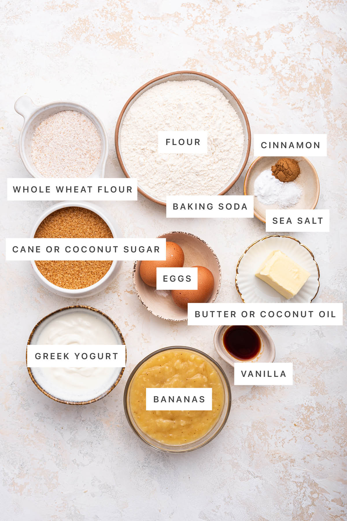 Ingredients measured out to make Healthy Banana Bread: whole wheat flour, flour, cinnamon, baking soda, sea salt, cane or coconut sugar, eggs, butter or coconut oil, vanilla, Greek yogurt and bananas.