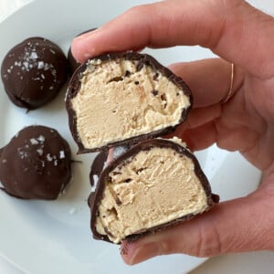 A woman's hand holding a peanut butter greek yogurt bite that is cut in half.