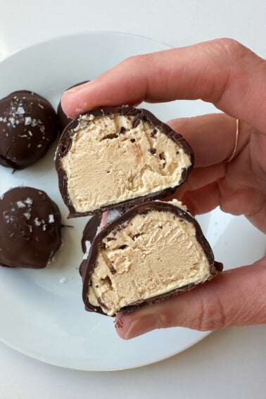 A woman's hand holding a peanut butter greek yogurt bite that is cut in half.