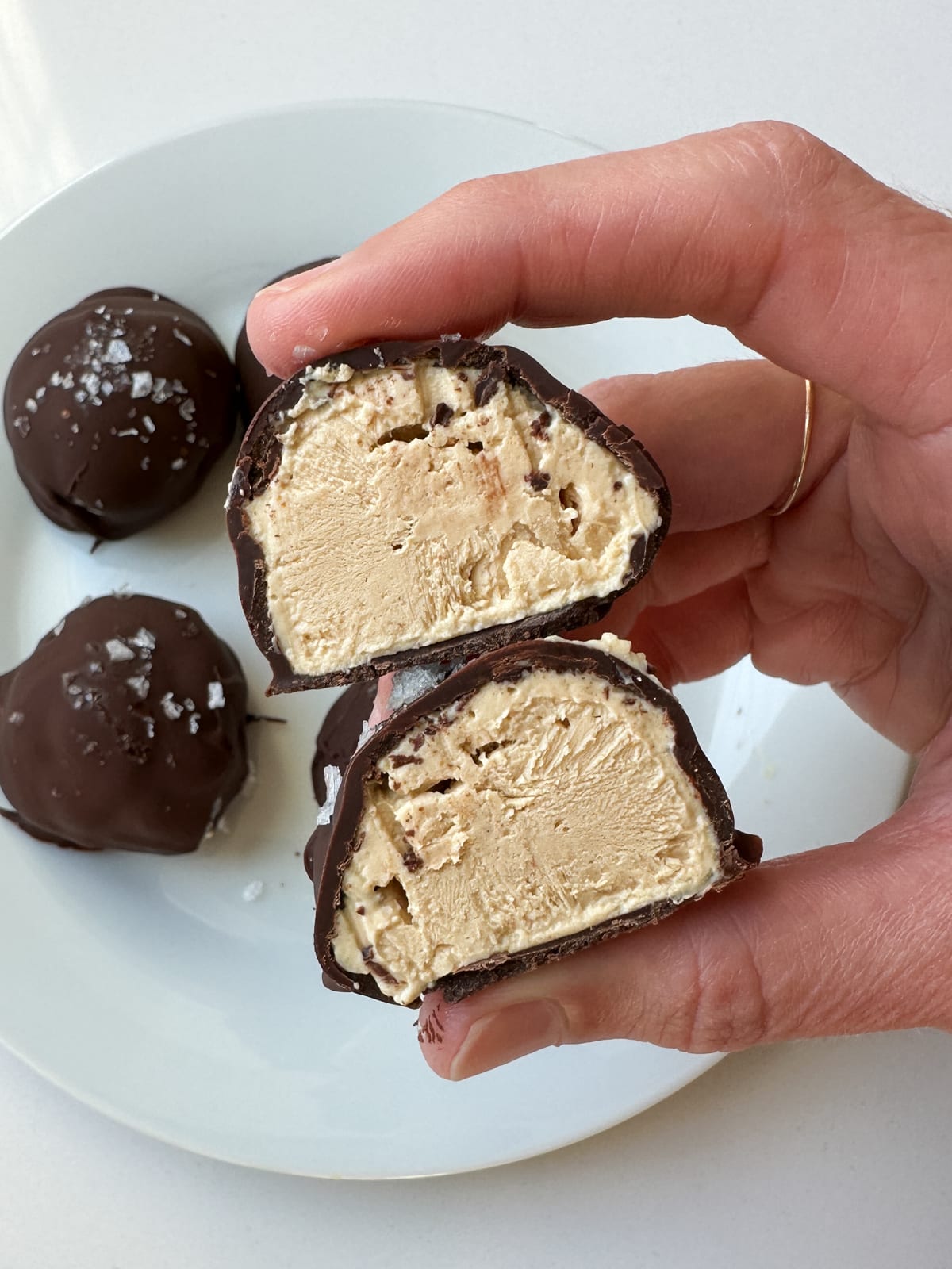 A woman's hand holding a peanut butter greek yogurt bite that is cut in half.