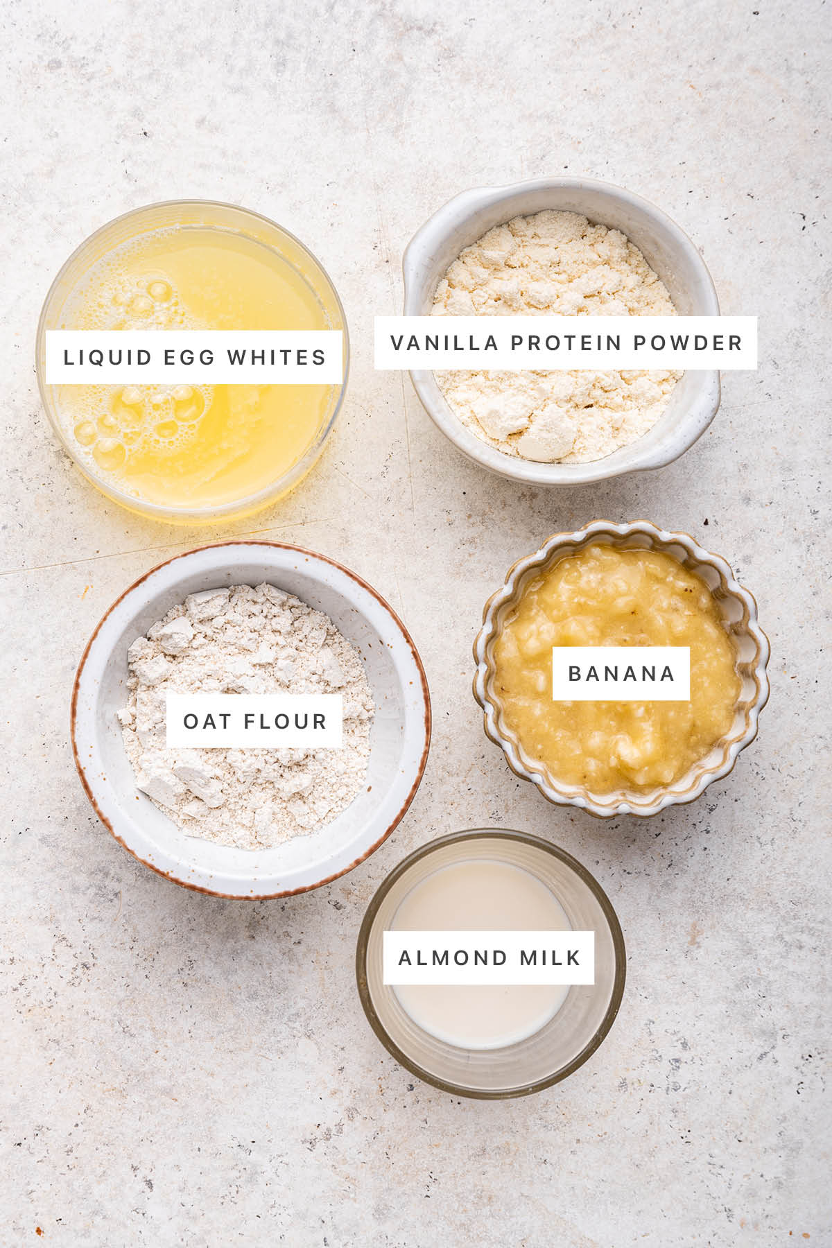 Ingredients measured out to make Protein Pancakes: liquid egg whites, vanilla protein powder, oat flour, banana and almond milk.