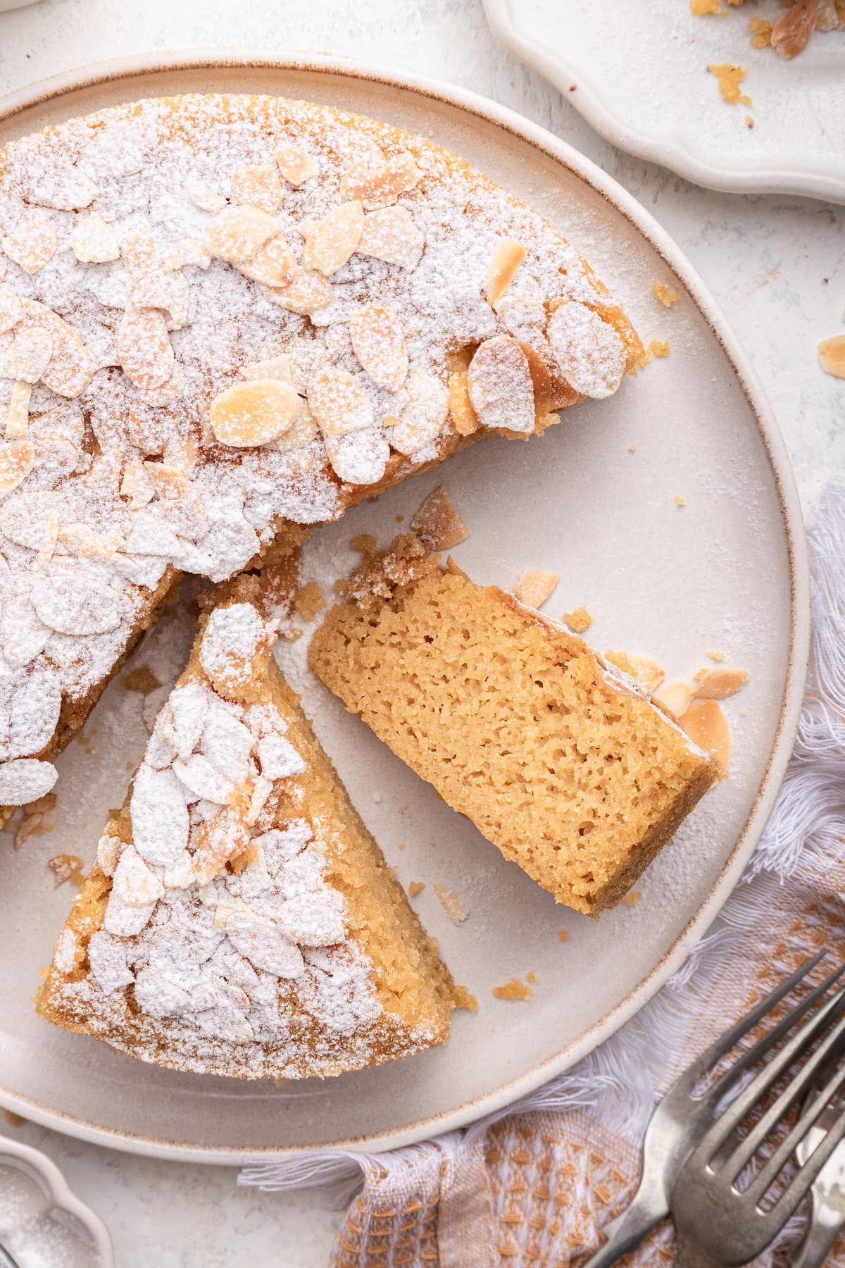 Almond cake on a large plate with three slices cut from the cake, and two of the slices are still on the plate.