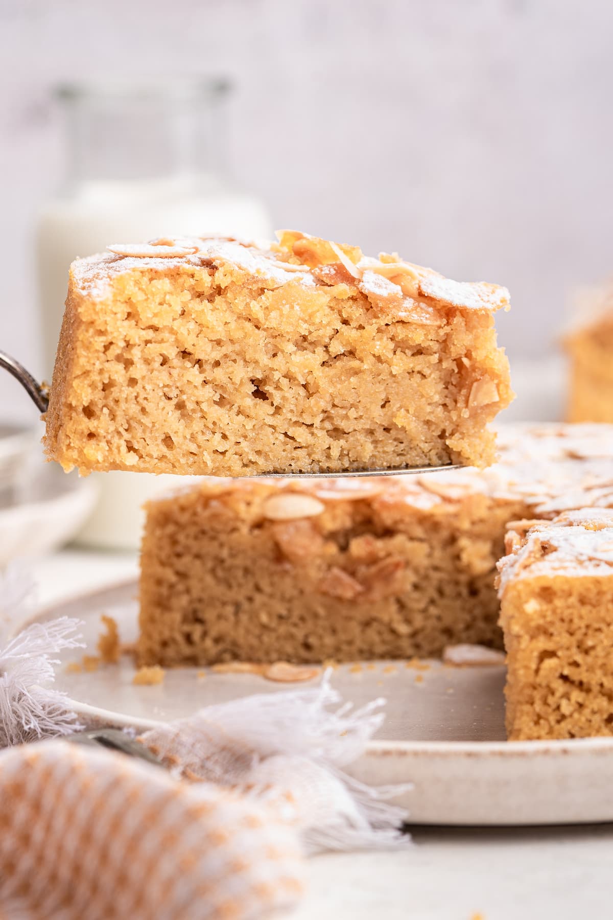 A slice of almond cake being lifted from a large plate by a metal spatula.