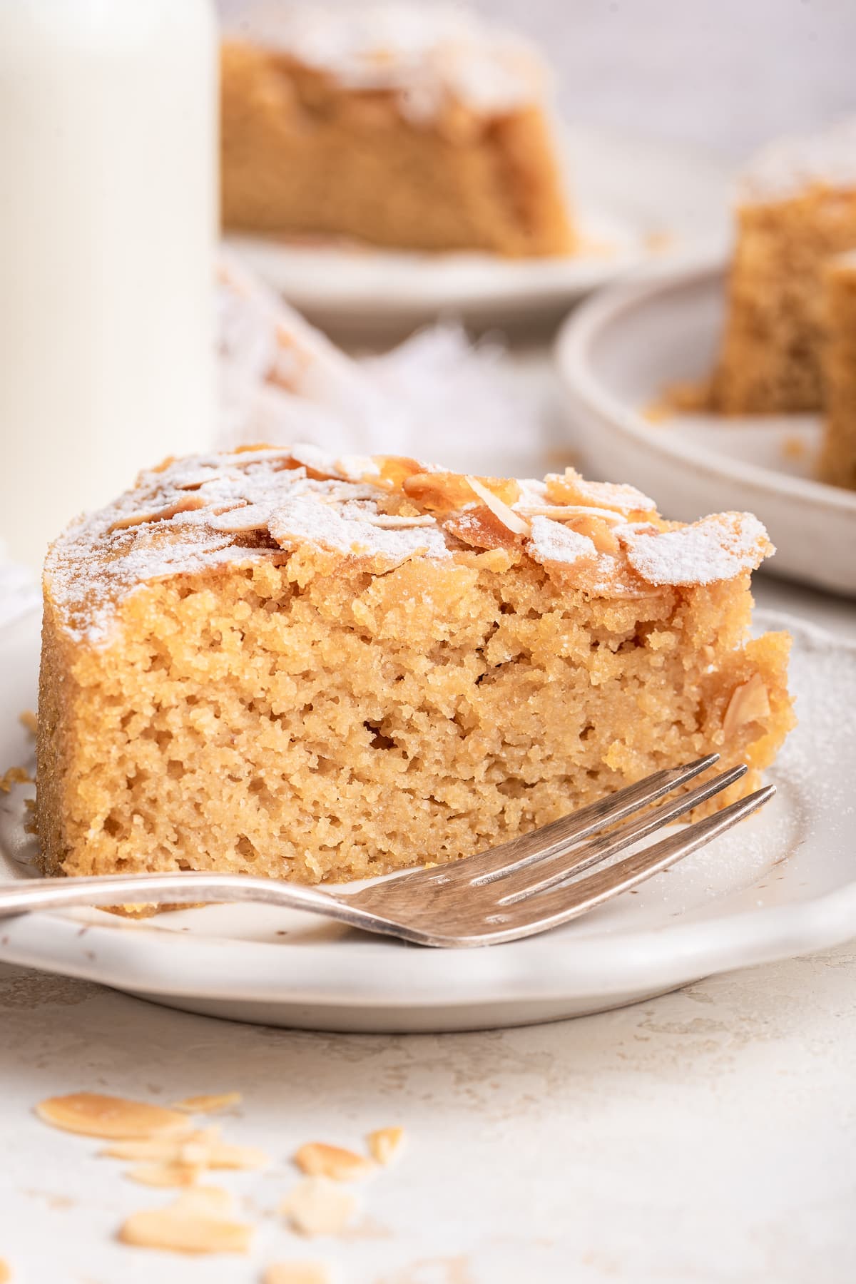 A slice of almond cake on a small plate near a metal fork.