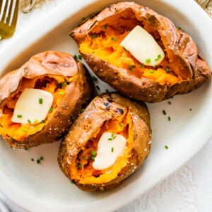 Three baked sweet potatoes split open with butter inside.