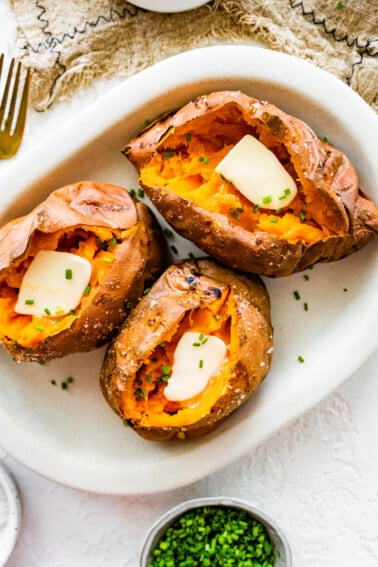 Three baked sweet potatoes split open with butter inside.