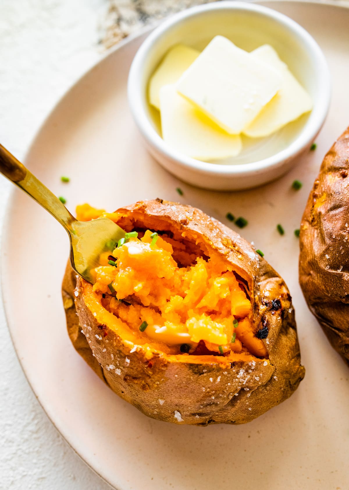 A fork inside a baked sweet potato that is on a plate.