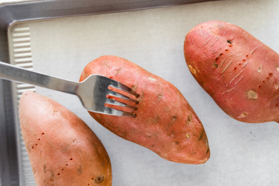A fork poking holes into a sweet potato.