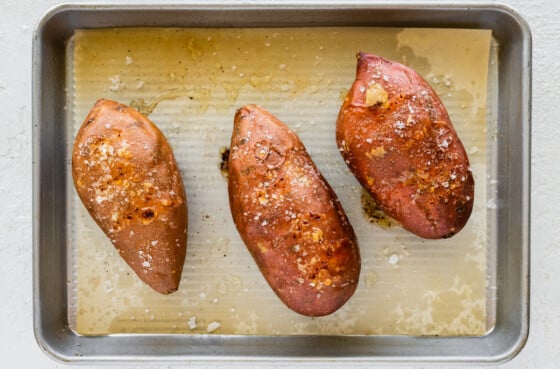 Three sweet potatoes on a baking tray after being baked in the oven.