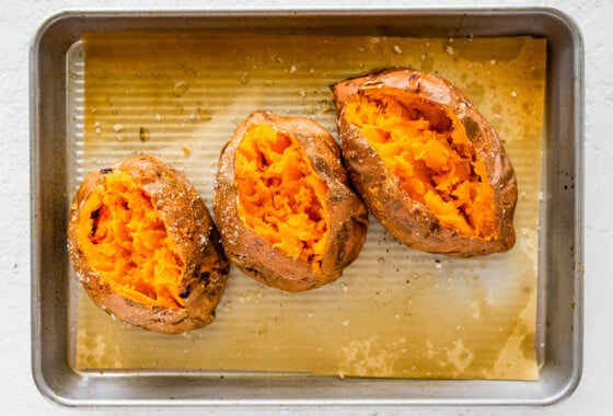 Three baked sweet potatoes split open on a baking tray.
