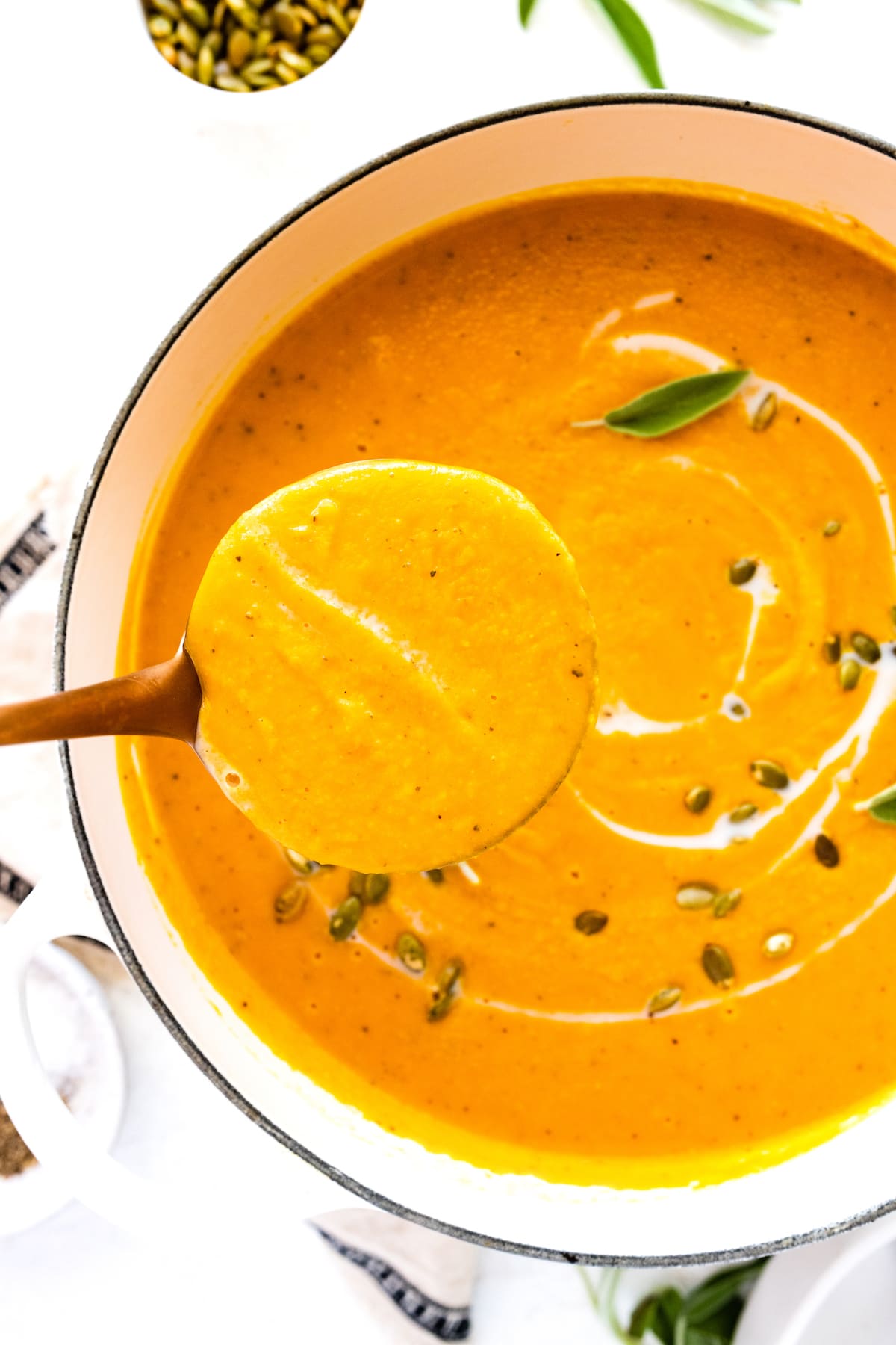 A wooden spoon holding a small portion of butternut squash soup of a large pot of soup.