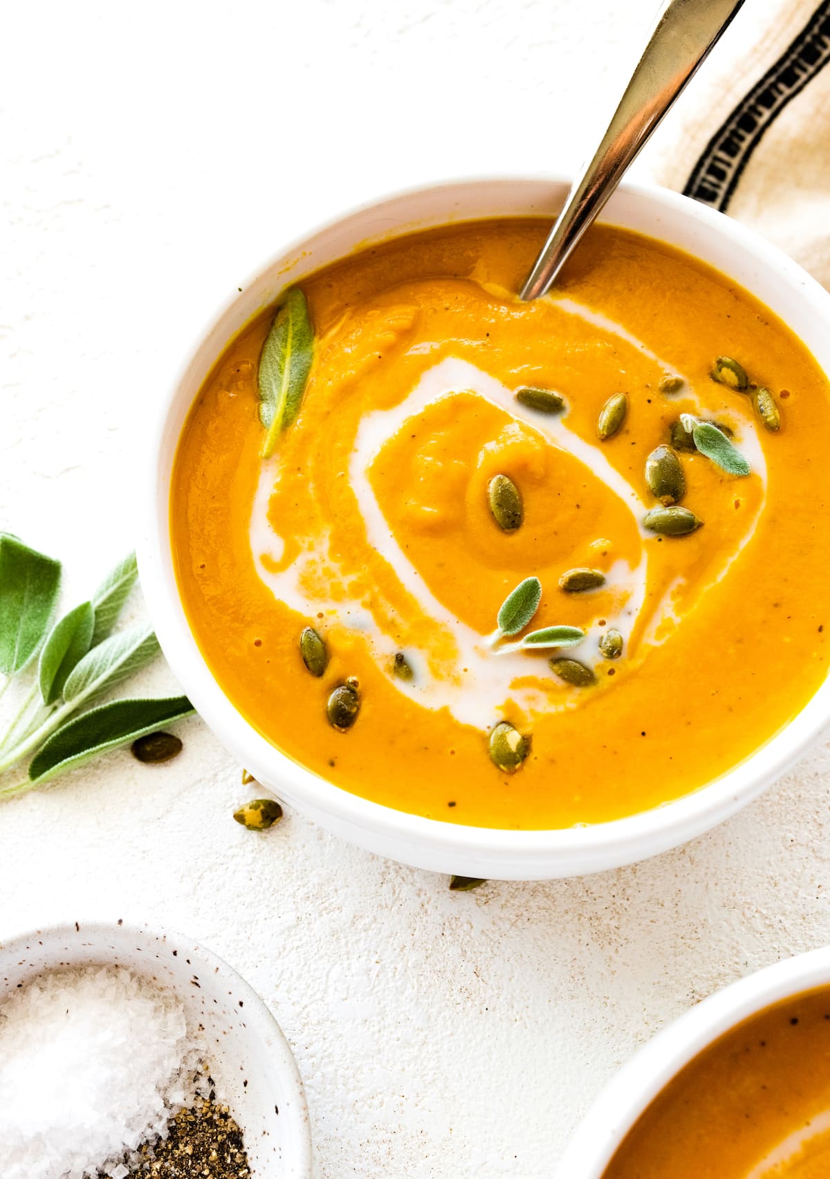 Butternut squash soup in a bowl garnished with coconut milk, pumpkin seeds, and fresh sage.