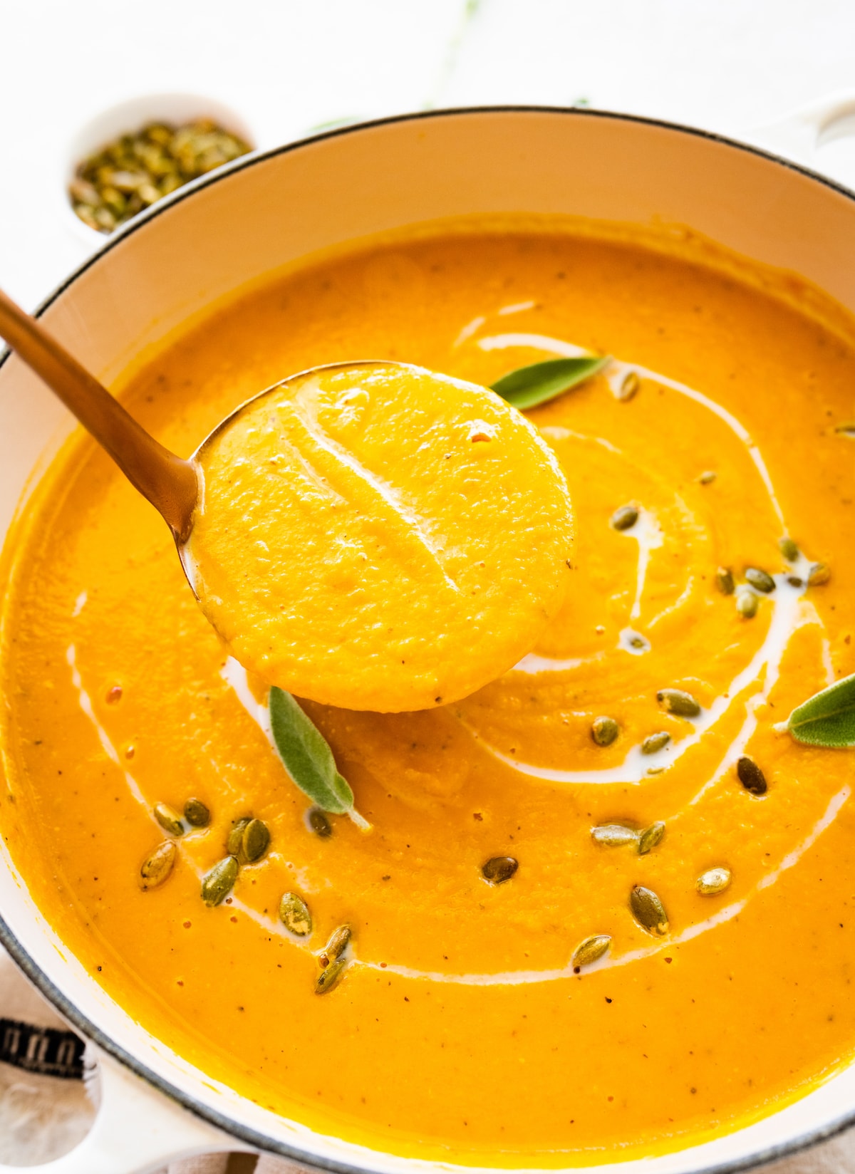 A ladle holding a portion of butternut squash soup over a large pot of the soup.