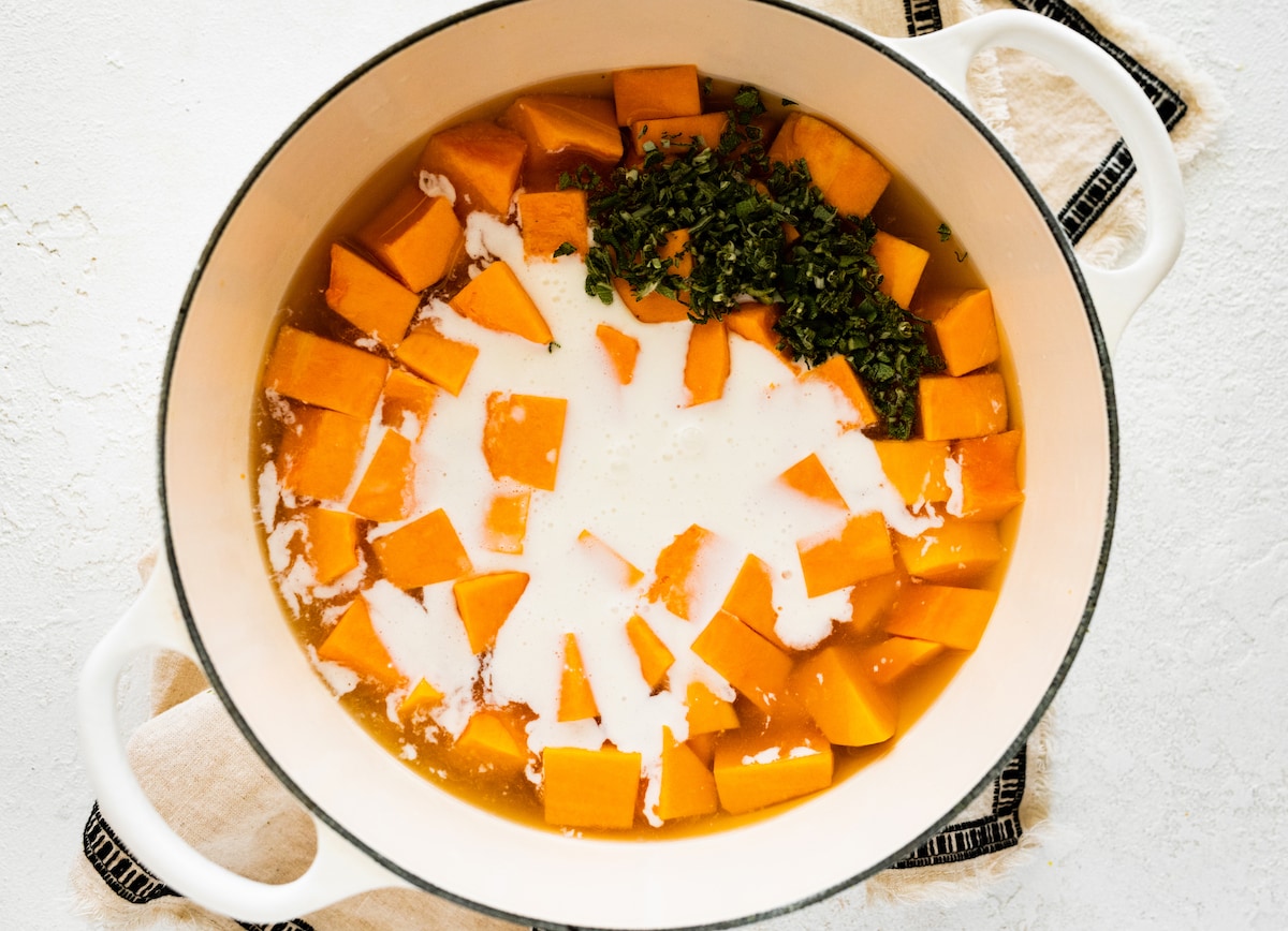 Cubed butternut squash, broth, and coconut milk added to a large pot to make the butternut squash soup.