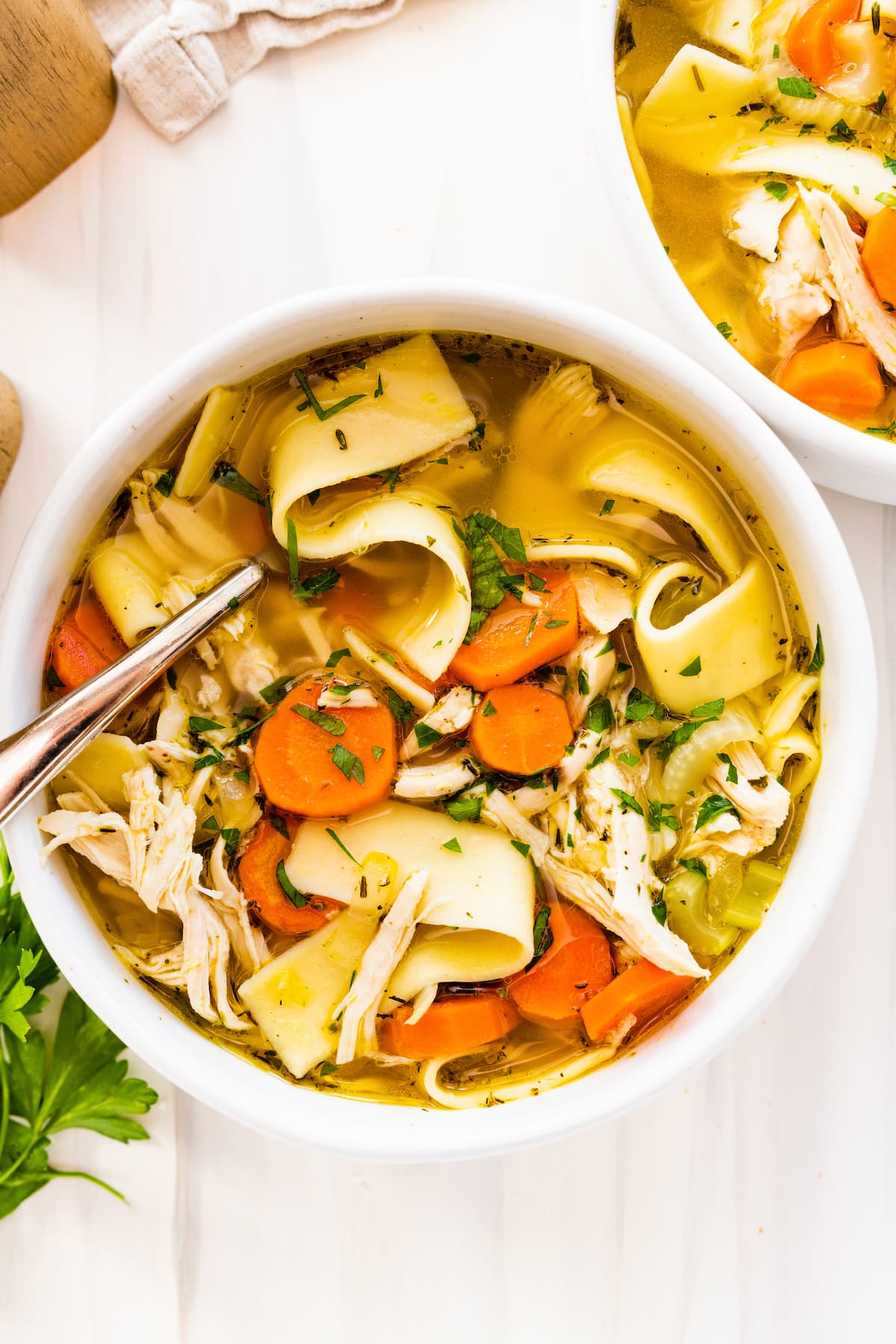 Chicken noodle soup in a white bowl with a metal spoon.