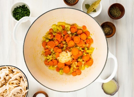 Veggies that include carrots, celery, onion, and garlic in a large pot.