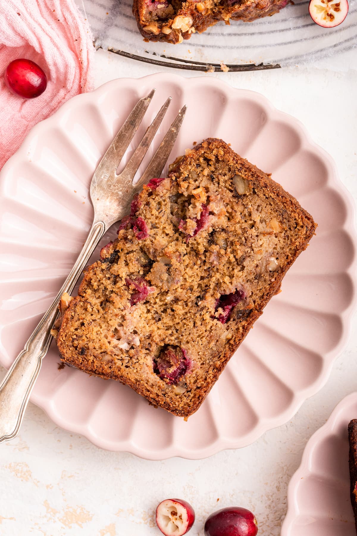 A slice of cranberry banana bread on a small plate with a metal fork.