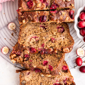 Three slices of cranberry banana bread leaning on one another near the loaf of bread.