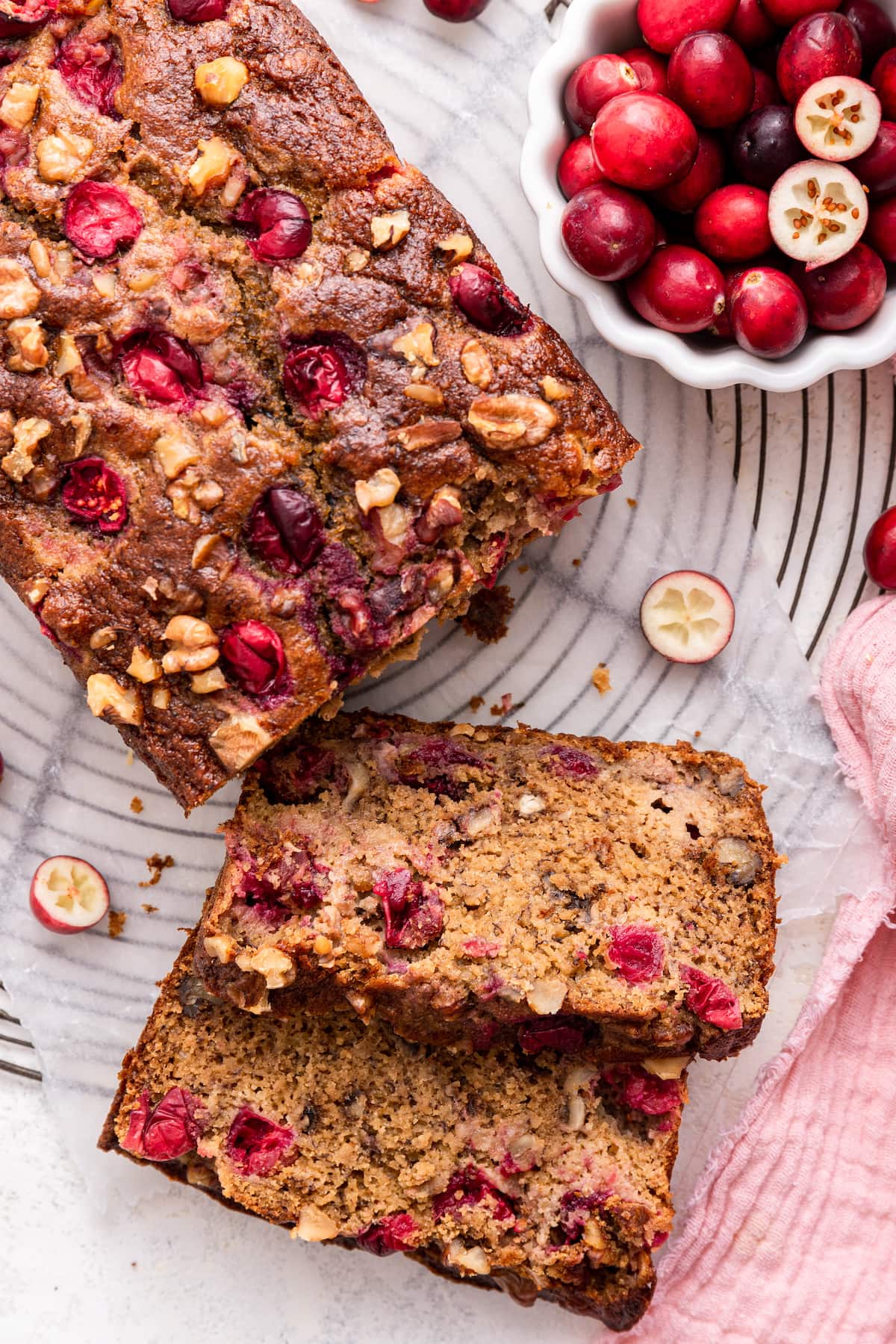 Two slices of cranberry banana bread near the loaf of bread.