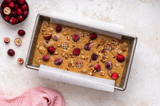 Cranberry banana bread dough topped with fresh cranberries in a loaf pan before being baked.