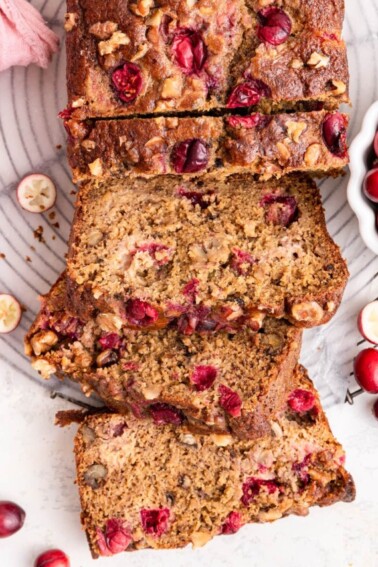 Three slices of cranberry banana bread leaning on one another near the loaf of bread.