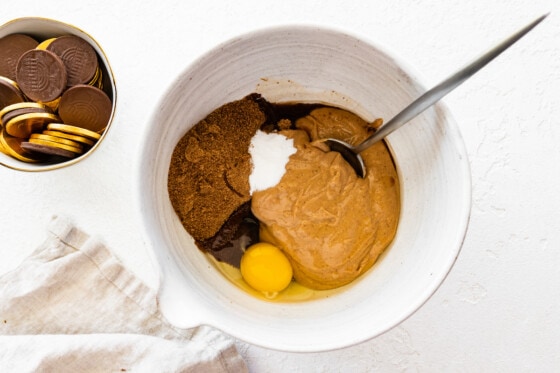 Preparing the batter for the peanut butter blossoms in a large mixing bowl. Ingredients include peanut butter, coconut sugar, an egg, vanilla, and baking soda.