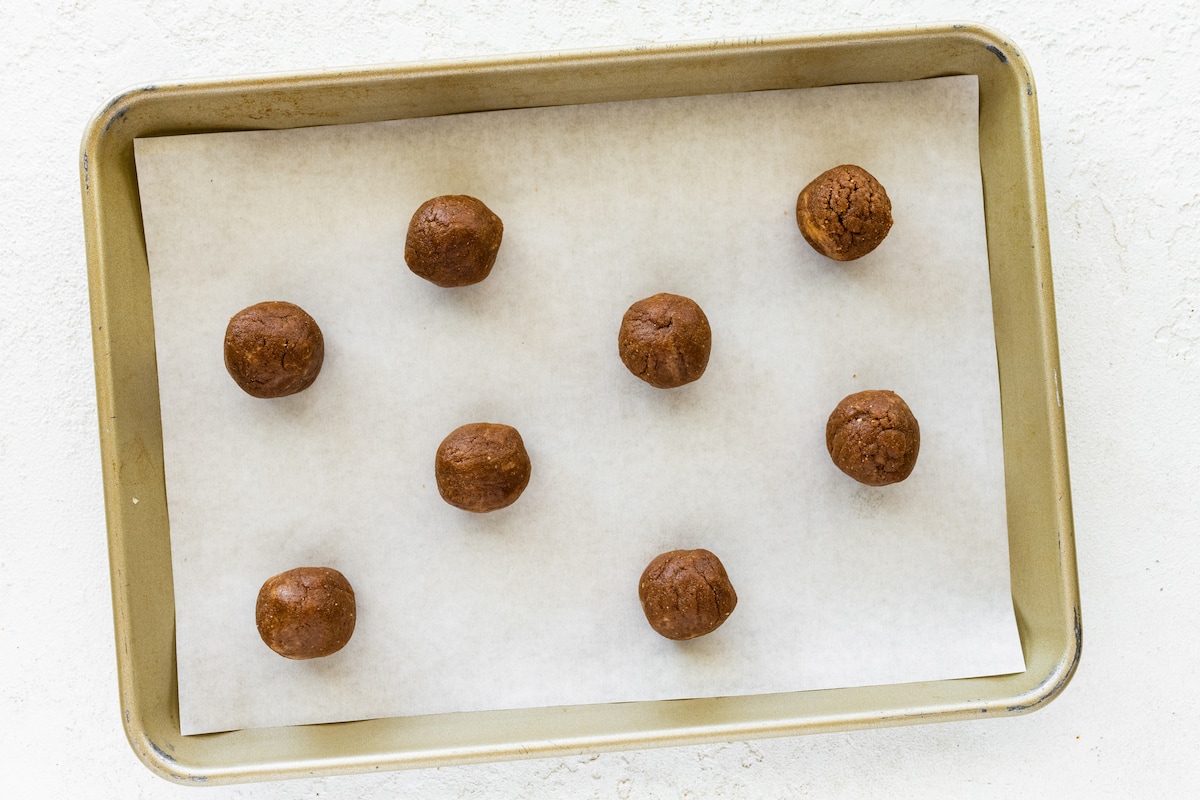 Peanut butter blossom balls on a baking sheet before being pressed into cookie shapes.