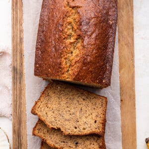 Banana bread on a wooden cutting board near three slices of the banana bread.