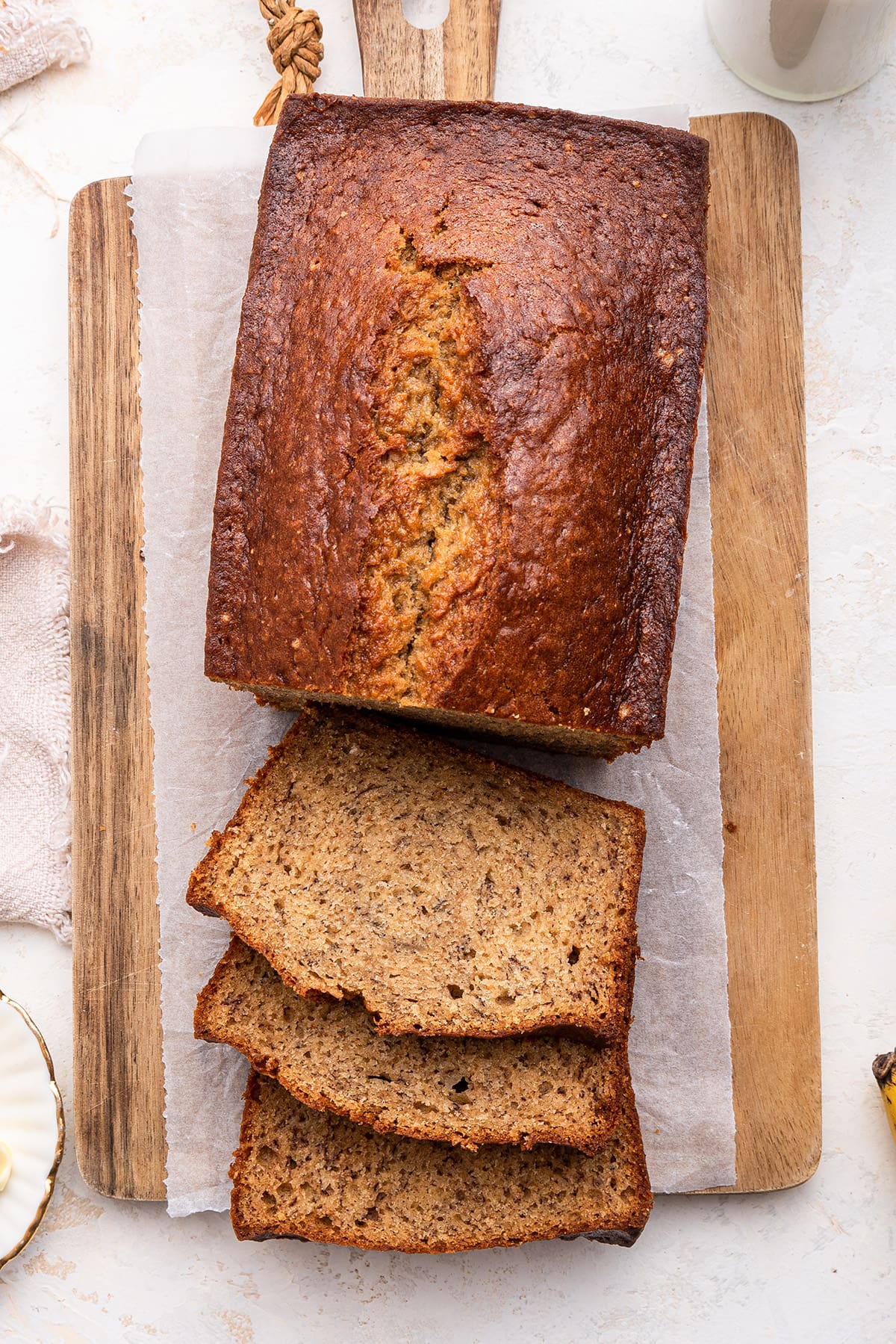 Banana bread on a wooden cutting board near three slices of the banana bread.