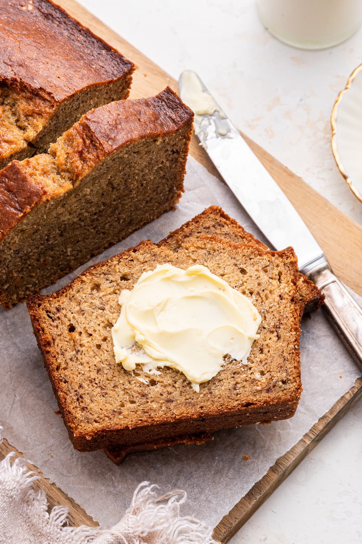 Two slices of banana bread stacked on one another on a wooden cutting board. The top slice has a dollop of butter.