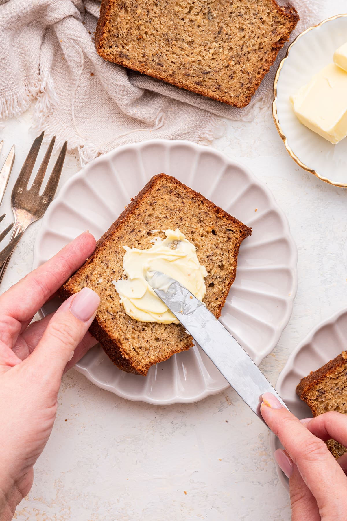 A woman uses a knife to spread butter on a slice of banana bread.