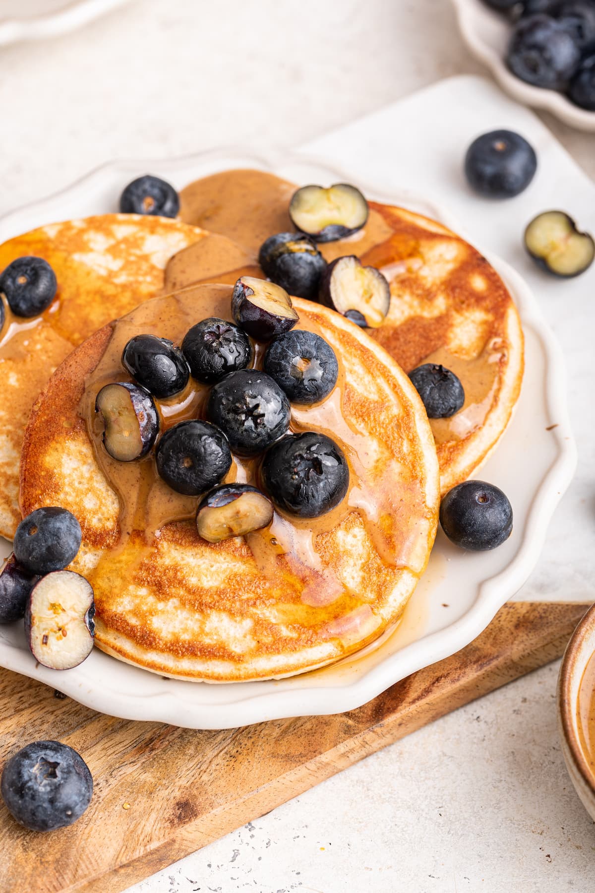 Three protein pancakes on a plate topped with maple syrup, fresh blueberries, and nut butter.