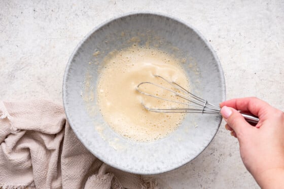 A woman's hand uses a metal whisk to create a protein pancake batter.